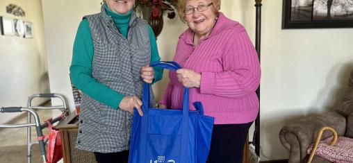 Two women smile while holding a Cedar Rapids Public Library book bag.