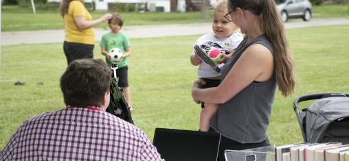 A woman holds a child in front of a library table in a park.