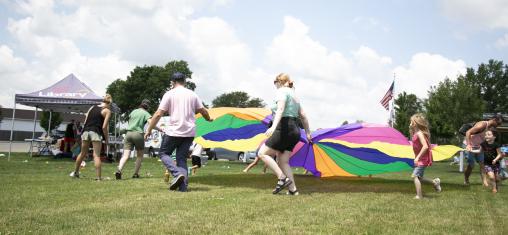 Children and adults hold a colorful parachute in a park.