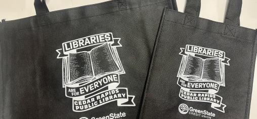 Two black tote bags say "Libraries are for Everyone" around a book illustration.