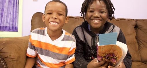 Two boys hold books and smile.