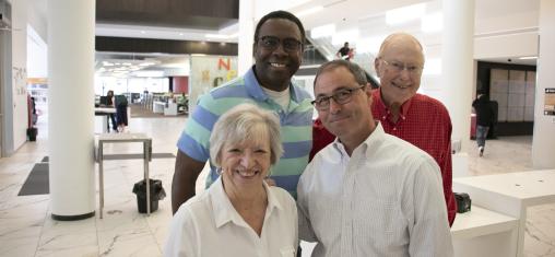 Four people smile in the Commons of the Downtown Library.