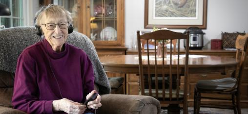 Maxine Valenta, age 93, wears headphones for an audiobook player while sitting in her living room.