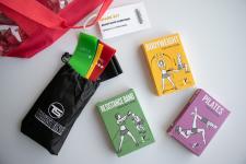 Colorful resistance bands in a black bag and exercise books sit on a white table.
