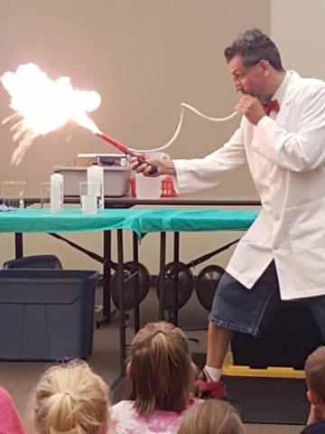Man in lab coat blowing on tube creating ball of fire