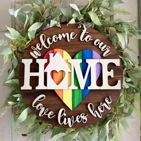 wooden wreath with the words "welcome to our home love lives here" in front of a rainbow heart.