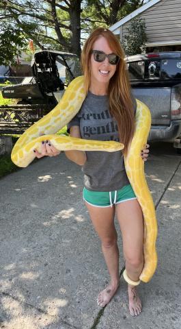 Lindsay McDermott has a large yellow snake over her shoulders, hanging to the ground, its tail around her ankle.
