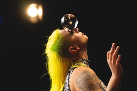 A woman, Sam Rezz, balances an orb on her face.