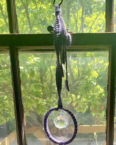 purple macrame hoop with prism in center hanging in window