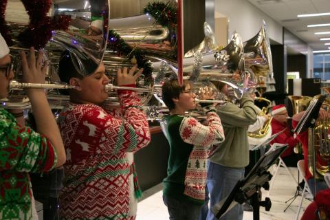 Teens in Christmas sweaters play brass instruments.