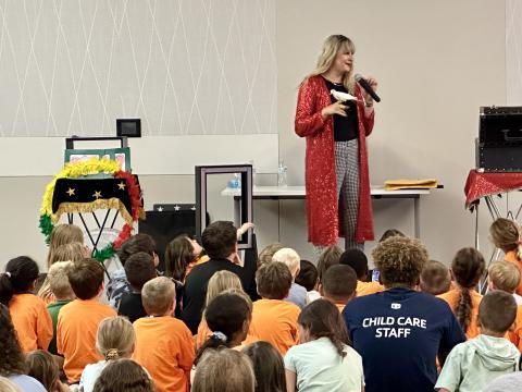 Mikayla Oz, wearing a long red coat, holds Bubbles the Bird, a dove, while children watch.