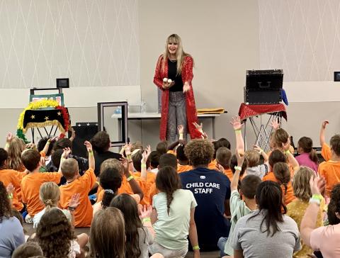 Mikayla Oz, wearing a long red coat, holds Bubbles the Bird, a dove, while children raise their hands.