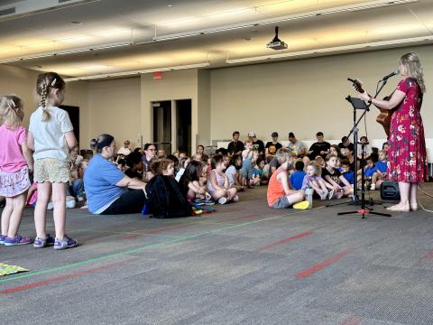 Amber Hansen plays a guitar and sings as children watch.