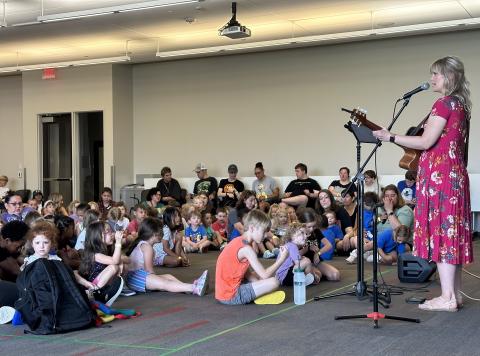 Amber Hansen plays a guitar and sings as children watch.