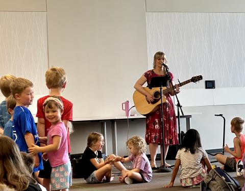 Amber Hansen plays a guitar and sings as children dance.