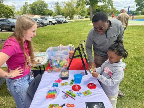 A child looks at prizes with an adult behind her, while a library staff member smiles from behind a table.