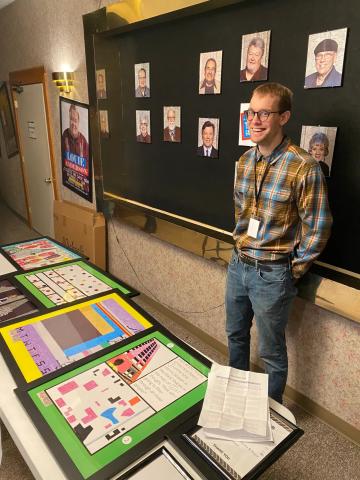 A man, Leo Bird, smiles behind a table with his art, which has bright geometric patterns.