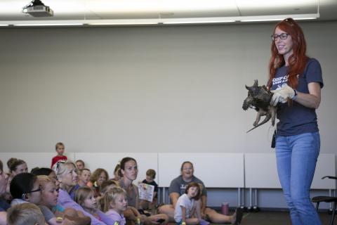 A red-headed woman shows a snapping turtle with an open mouth to watching children.