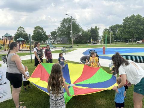 Children and adults hold on to all sides of a giant parachute at Redmond Park.