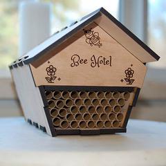 A pentagram shaped box that looks like a home is halfway filled with small cardboard tubes and is engraved with "bee hotel" above the tubes.