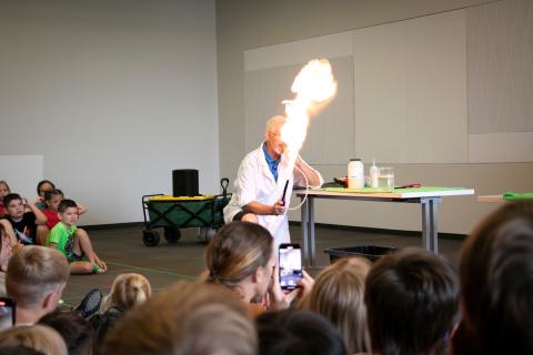 Children watch as a man in a lab coat blows a fire ball.