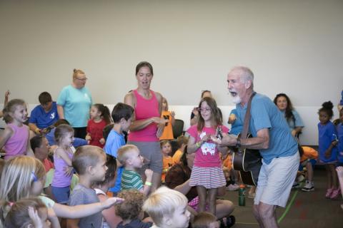 Tom Pease plays the guitar as children watch.