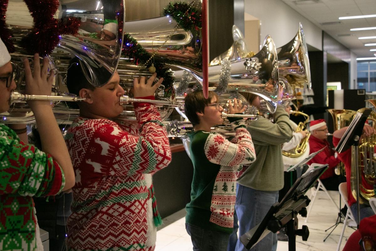Teens in Christmas sweaters play brass instruments.
