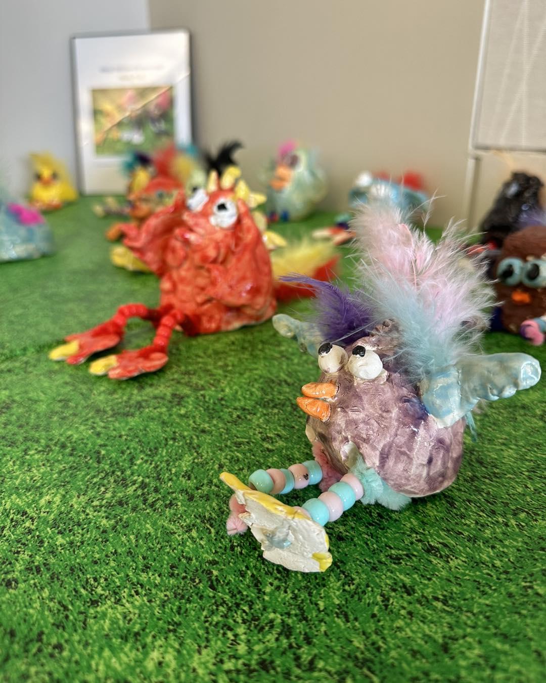 A clay creature with feathers, big blue ears, a purple head, and beads for legs.