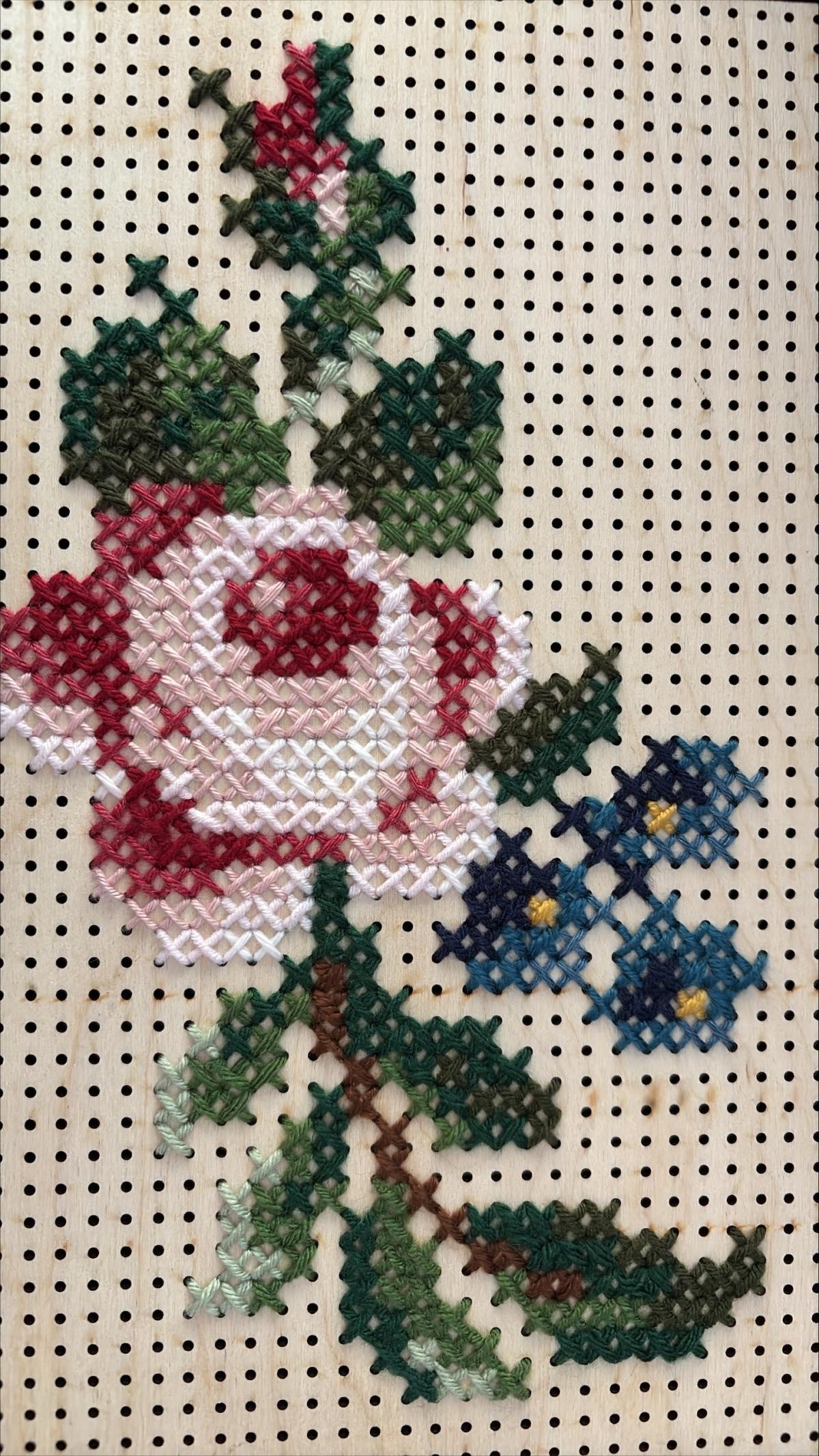 rose cross stitch on a piece of wood with holes