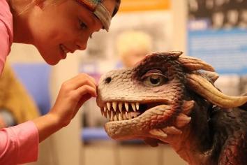 child touching the nose of a life-like dragon puppet