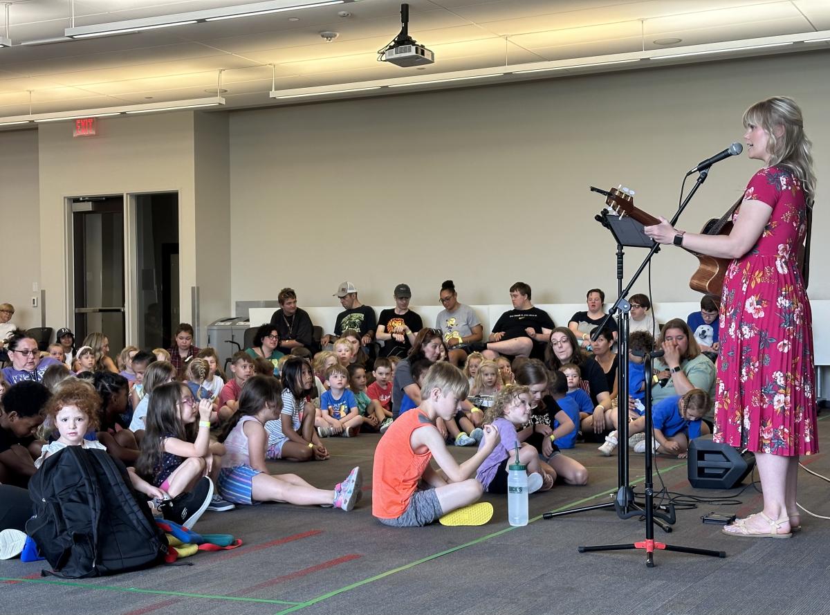 Amber Hansen plays a guitar and sings as children watch.