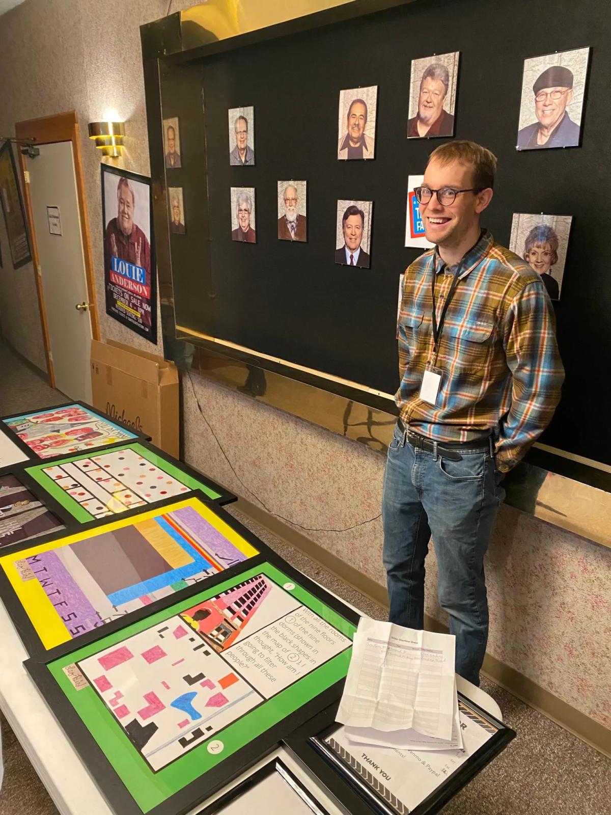 A man, Leo Bird, smiles behind a table with his art, which has bright geometric patterns.