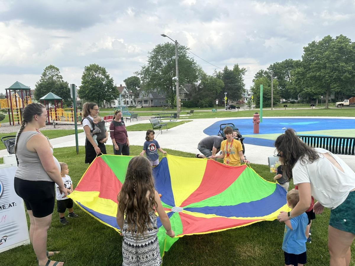 Children and adults hold on to all sides of a giant parachute at Redmond Park.