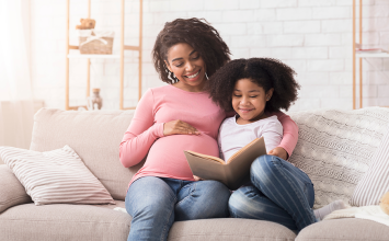 Pregnant woman with young daughter reading together on couch