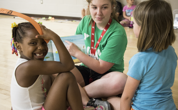 Librarian reading to two young girls, one looking at the camera with a smile