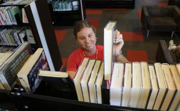 A woman in a red shirt shelves books.