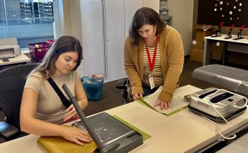 Two women work on preparing gold vinyl for a Cricut design.