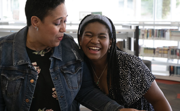 A woman and a girl laugh in the library.