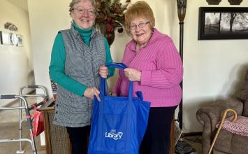 Two women smile while holding a Cedar Rapids Public Library book bag.